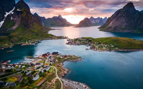 En pittoresk by med röda hus vid en fjord, omgiven av dramatiska berg. En av de fina platserna i Norge, badande i solnedgångens ljus.
