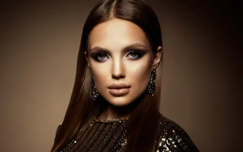 Mujer con un look de **soft goth makeup**, ojos ahumados y labios definidos, luciendo pendientes largos y un vestido brillante.