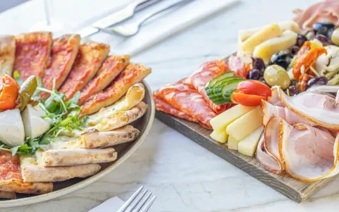 Talerz z pizzą i deska serów z wędlinami, oliwkami i pomidorkami.