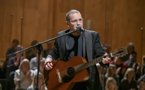Artysta z gitarą i mikrofonem na scenie podczas koncertu Męskie Granie w Poznaniu.