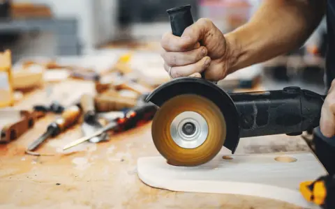 Mano trabajando con amoladora, mostrando sus usos en carpintería para dar forma a la madera.