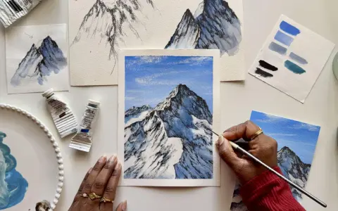 Une main peint une peinture montagne facile, avec des tubes de peinture et des nuanciers bleus à proximité.