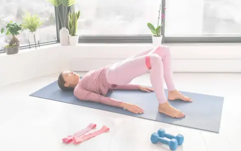 Femme faisant un pont avec une bande de résistance pour comment muscler les fessiers. Haltères et bandes roses à proximité.