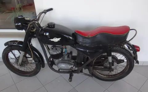 Czarny motocykl wsk 125 z czerwoną kanapą, stojący na szarej podłodze.