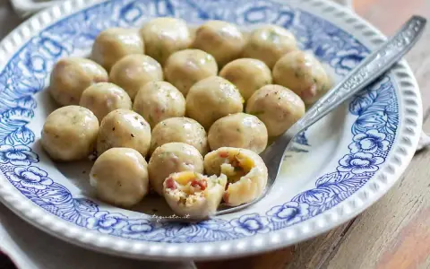Gnocchi di pane saporiti, serviti su un piatto decorato. Uno è tagliato a metà, rivelando un ripieno gustoso.