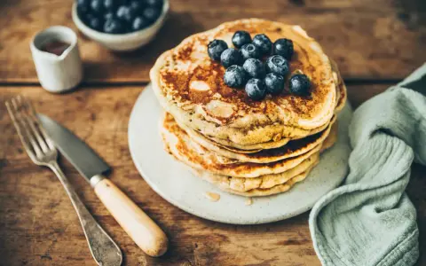 Pile de pancakes au levain garnis de myrtilles, sur une assiette, avec une fourchette et un couteau.