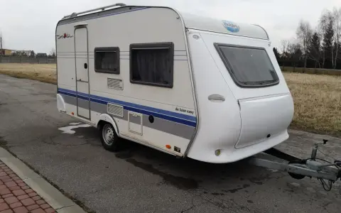 Biała przyczepa kempingowa Hobby 400 de luxe easy z niebieskimi pasami, gotowa na wakacyjne podróże.