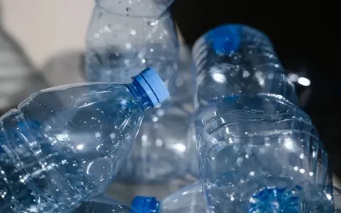 Stos pustych, przezroczystych butelek PET z niebieskimi nakrętkami, gotowych do recyklingu.