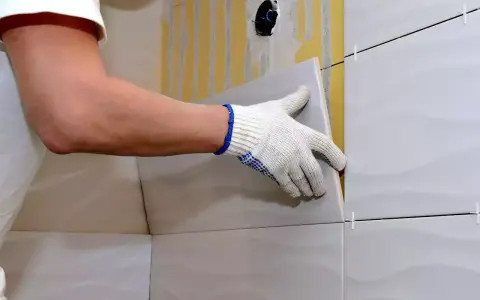 Man con guantes coloca una baldosa nueva sobre un alicatado existente.