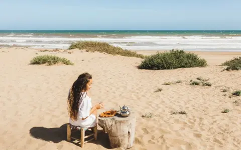 Kobieta pije herbatę na piaszczystej plaży, delektując się widokiem na turkusowe tunezyjskie morze.