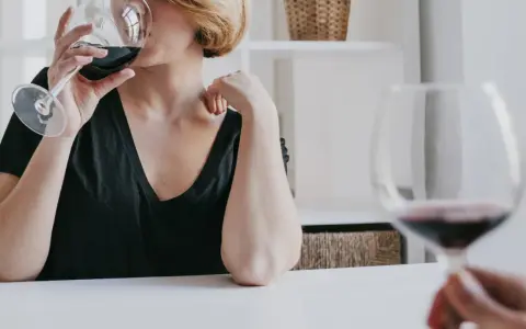 Kobieta z krótkimi blond włosami pije czerwone wino. Czy zastanawiasz się, jak hashimoto a alkohol wpływają na zdrowie?