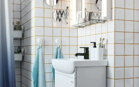 Salle de bain moderne avec carrelage blanc et joints dorés, évier, robinetterie noire et accessoires. Idéal pour un plancher chauffant avec un joint de 2mm.