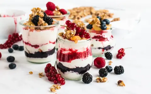 Leckeres Dessert mit Beeren und Joghurt in Gläsern geschichtet, garniert mit Granola und frischen Früchten.