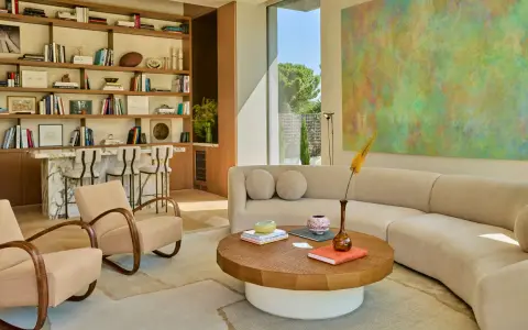 Sofá curvo y sillones de diseño contemporáneo, estanterías llenas de libros y arte abstracto en un salón luminoso.