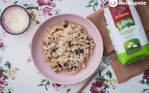 Arroz meloso con berenjenas en plato rosa, acompañado de queso rallado y bolsa de arroz Sabroz.