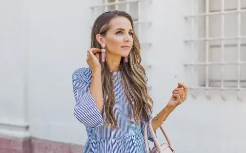 Mujer con un vestido de rayas azules y blancas, mangas acampanadas y pendientes rosas.