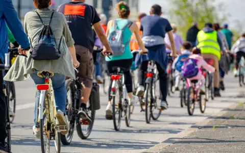 Grupa rowerzystów jedzie w kolumnie, przestrzegając przepisów. Widać plecaki i kamizelki odblaskowe.