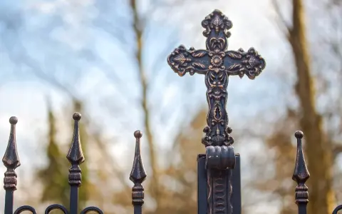 Krzyż na metalowym ogrodzeniu, symbol nadziei i walki z siedmioma grzechami głównymi.