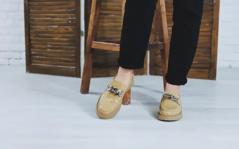 Beżowe, lakierowane buty bez skarpet z ozdobnym łańcuchem, idealne do czarnych spodni.