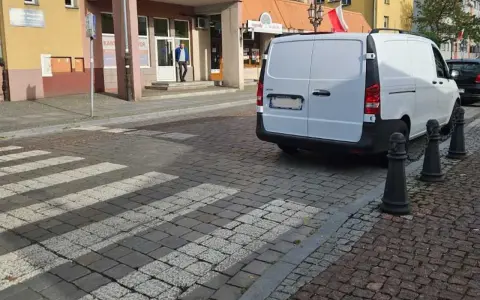 Biały van blokuje przejście dla pieszych na brukowanej ulicy.