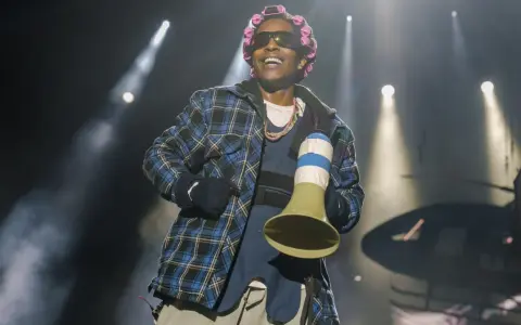 A$AP Rocky na koncercie w kręconych włosach i kratowanej koszuli, trzymający megafon.