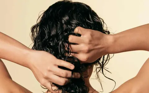 Manos peinando cabello oscuro y rizado, con un toque de cabello esponjado.