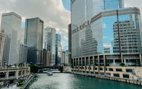 Chicago's iconic skyline along the river, with the Trump Tower reflecting the clouds. A boat glides by, making you wonder, is Chicago worth visiting?