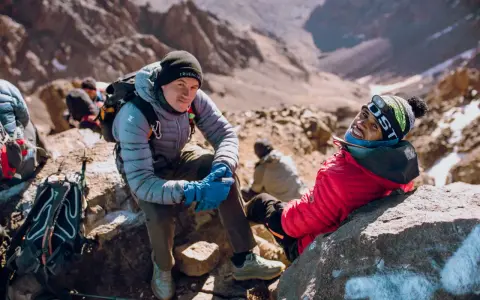Uśmiechnięci alpiniści podczas wyprawy na Toubkal. W tle skaliste zbocza górskie.