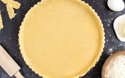 Ein vorbereiteter Mürbeteigboden in einer Tarteform, bereit für das 1 2 3 Teig Rezept. Zutaten wie Eier, Butter und Mehl sind daneben zu sehen.