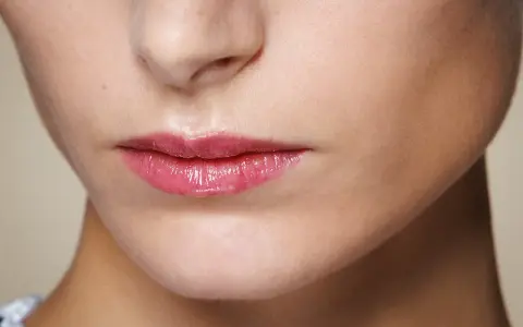 Labbra sottili e lucide con un tocco di gloss rosa, che catturano la luce.