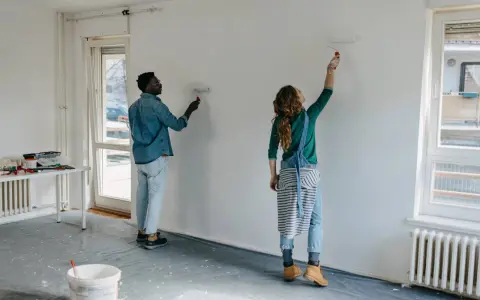 Pareja pintando una pared blanca, renovando su hogar. El hombre y la mujer usan rodillos para pintar sobre lacado, transformando el espacio.