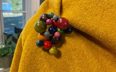En gul, ullig poncho med en klunga av färgglada träpärlor som en brosch. Perfekt för att sy en unik poncho.