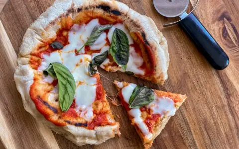 Pizza in padella appena sfornata, con pomodoro, mozzarella filante e basilico fresco, pronta per essere tagliata.