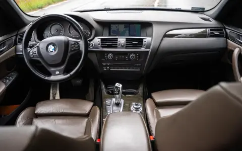 Wnętrze BMW X3 z brązową skórzaną tapicerką i drewnianymi wstawkami. Kierownica, deska rozdzielcza i nawigacja. Wiele osób szuka bmw x3 opinie, by poznać ten model.