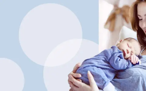 Uśmiechnięta mama tuli śpiącego noworodka w pasiastym pajacyku. Wskazówki, jak ubierać noworodka w domu.