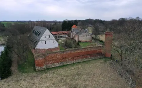 Zamek Kiszewski, z ceglanymi murami i wieżą, otoczony zielenią i drzewami.