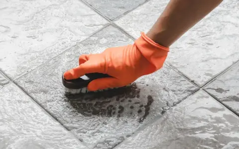 Mano con guante naranja cepillando un suelo antideslizante con espuma.