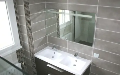 Salle de bain moderne avec double vasque. Le carrelage sol gris, posé au mur, crée une ambiance élégante.