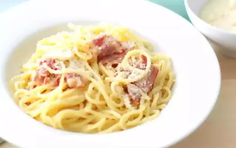 Une assiette de spaghetti crémeux, parsemée de lardons et de parmesan. La vraie recette carbonara italienne, un délice simple et authentique.