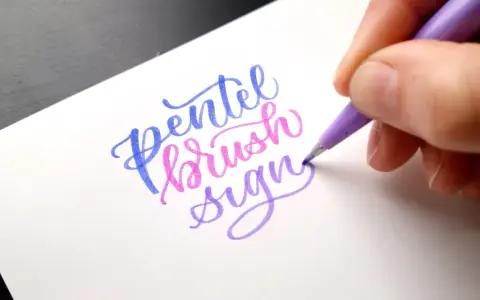 En hand skapar vacker brush lettering med en lila penna. Orden "Pentel brush sign" framträder i blått, rosa och lila.