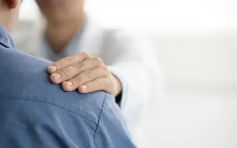 Dłoń lekarza na ramieniu pacjenta. Czy do psychiatry potrzebne jest skierowanie? Wsparcie i troska w gabinecie lekarskim.