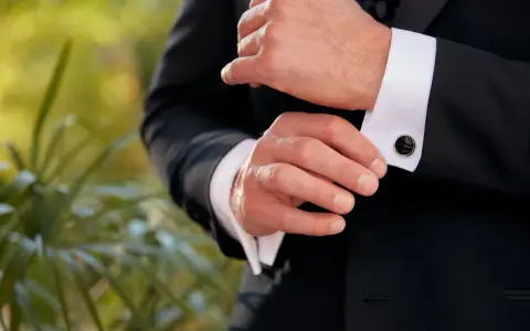 A man fastens his black cufflinks on his white shirt cuffs, completing his tux.
