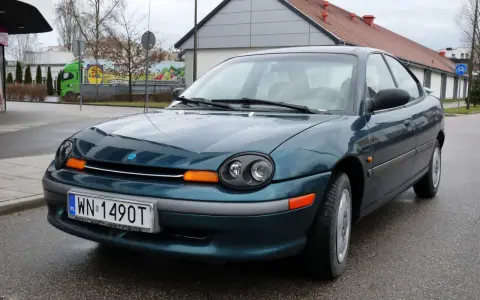 Zielony Dodge Neon z tablicą rejestracyjną WN 1490T stoi na mokrej drodze przed budynkiem.