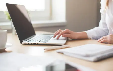 Mano su laptop, penna e quaderno. Ricerca su quanto guadagna un traduttore.