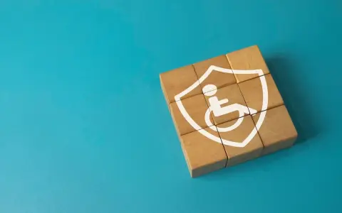 Drewniane klocki tworzą tarczę z symbolem osoby na wózku, symbolizującą ochronę w przypadku niepełnosprawności neurologicznej.