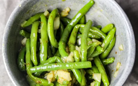 En skål med glansiga, gröna haricots verts blandade med bitar av vitlök och kryddor.