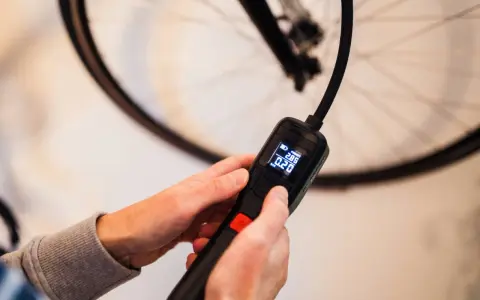 Hände halten eine digitale Luftpumpe, die den Druck in Bar anzeigt, bereit, den Fahrradreifen aufzufüllen.