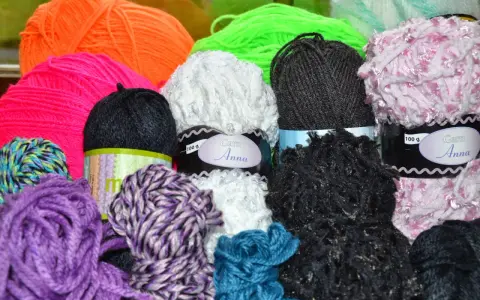 A colorful assortment of yarn balls in various textures and colors, including purple, pink, orange, green, white, black, and blue.
