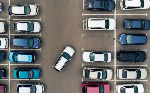 Widok z góry na parking z wieloma samochodami. Jeden biały samochód jest zaparkowany tyłem, pokazując, jak parkować tyłem.