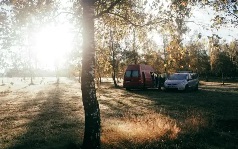 Sonnenaufgang im Herbst. Ein roter Camper und ein silberner Van stehen auf einer Wiese. Das ist Freiheit, das ist was ist wildcampen.